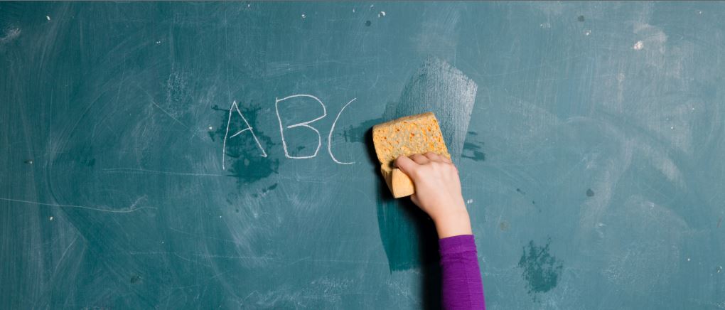 Eine Kinderhand wischt mit einem Schwamm eine Schultafel sauber.