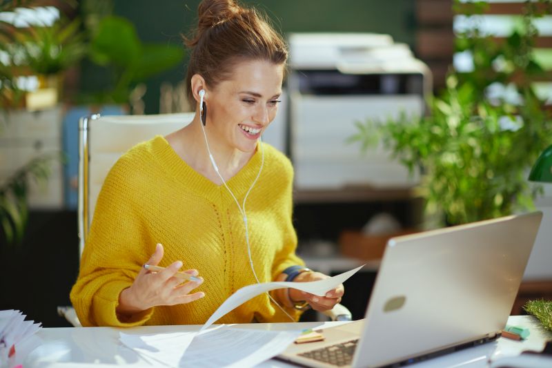 smiling elegant small business owner woman in yellow sweater with laptop having virtual meeting in the modern green office.