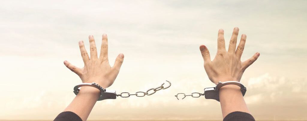 Zwei Hände mit gebrochenen Handschellen, die sich in den Himmel strecken.
