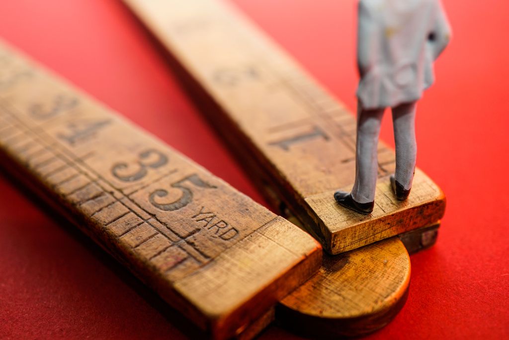 Eine winzige Figur eines Mannes steht auf der Spitze eines Holzlineals.