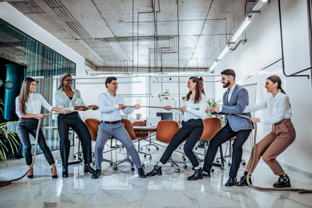 Geschäftsleute in einem modernen Büro beim Tauziehen – symbolisch für Teamarbeit und Wettbewerb.