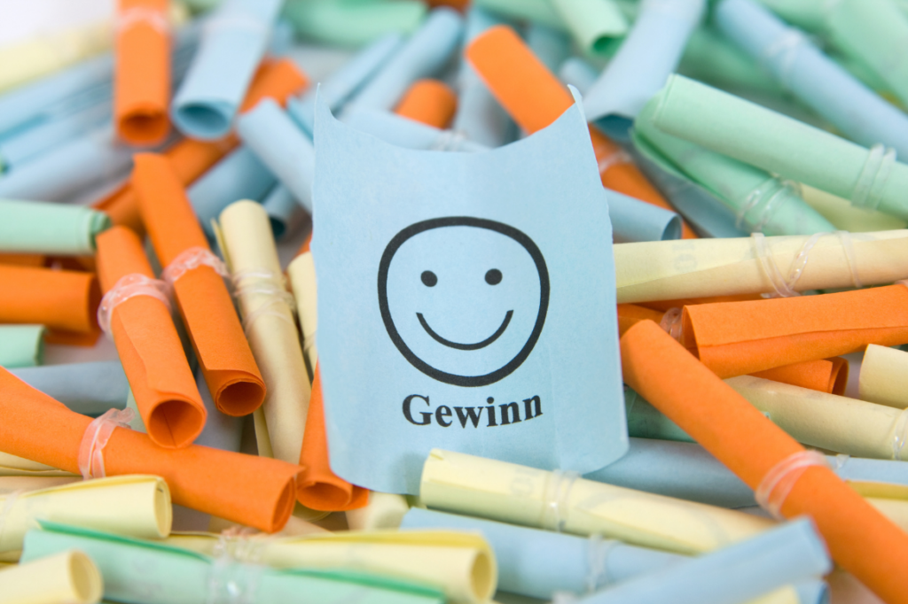 Viele bunte Papierlose, eines davon mit einem Smiley und der Aufschrift „Gewinn“.