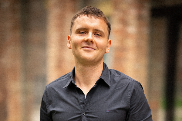 Porträt von Fabian Moling vor einer Ziegelwand, in dunklem Hemd, freundlich in die Kamera blickend.