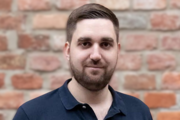 Porträt von Philipp Kamper vor einer Ziegelwand, freundlich in die Kamera blickend.