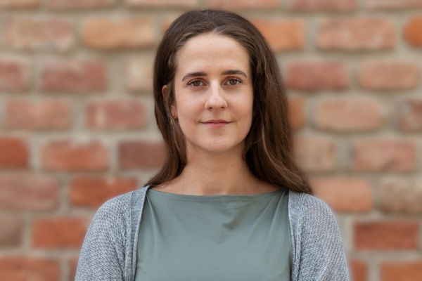 Porträt von Florentina Glüxam vor einer Ziegelwand, freundlich in die Kamera blickend.