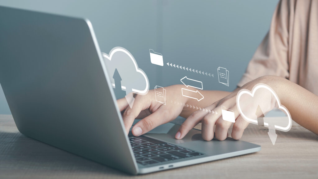 Hände tippen auf Laptop, Cloud-Symbole und Dateipfeile symbolisieren Datenübertragung in die Cloud.