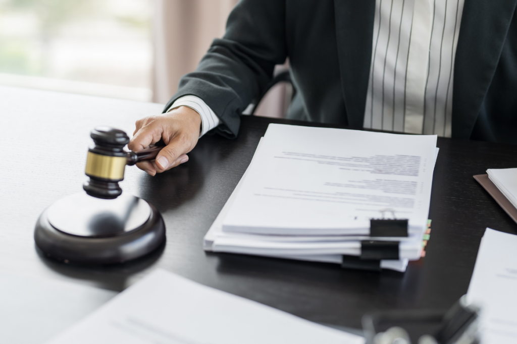 Person in Businesskleidung mit Richterhammer und Aktenstapel, Symbolbild für rechtliche Entscheidungen oder Vergabeverfahren.
